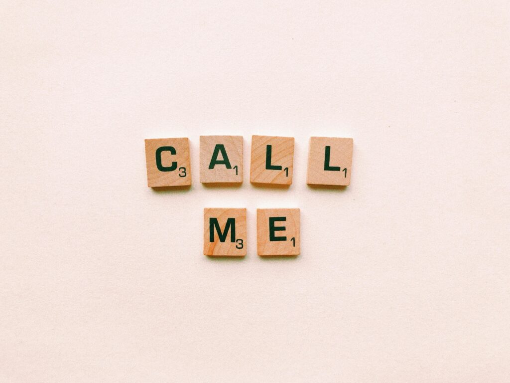 Wooden letter tiles spelling 'Call Me' on a pastel pink background, invoking communication and connection.