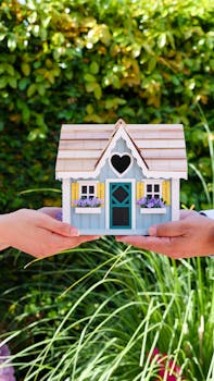 Two hands hold a colorful miniature house outdoors, symbolizing real estate and home ownership.